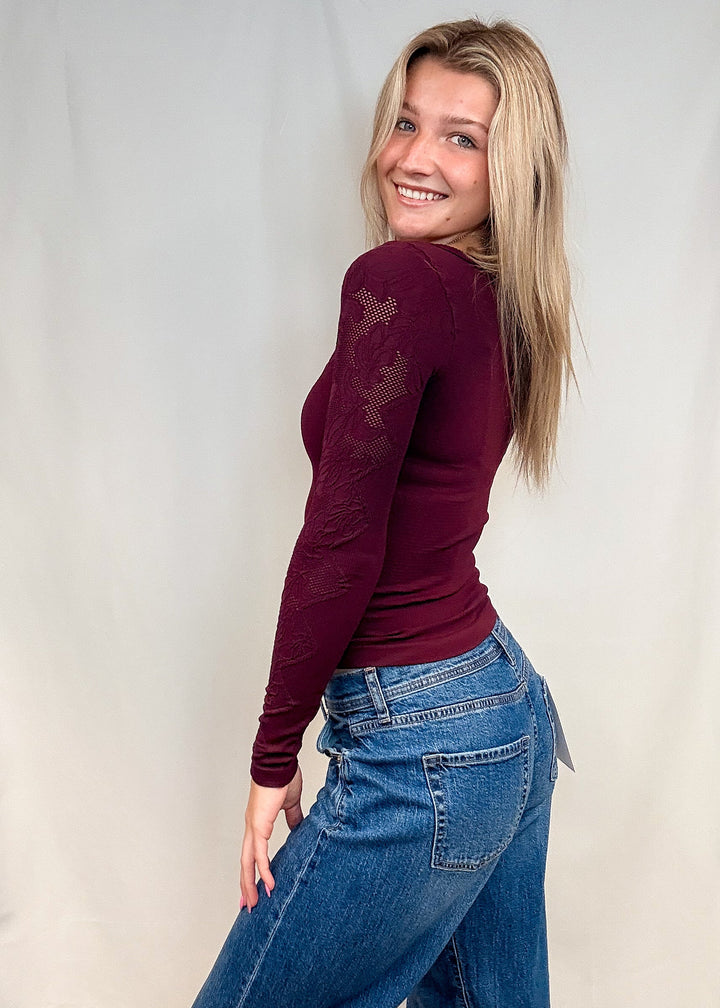 Woman wearing burgundy fitted lace top with blue jeans on white background