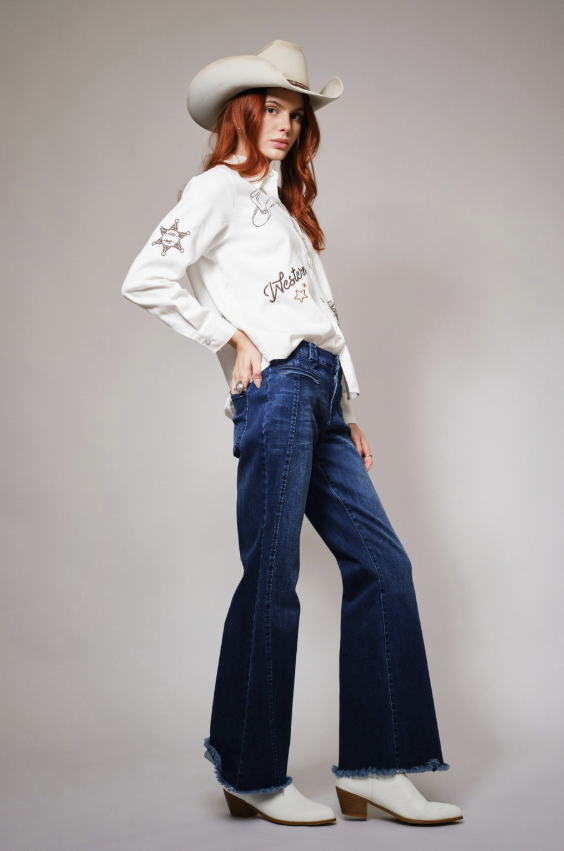 Woman wearing a white blouse, blue jeans, and a cowboy hat on a gray background