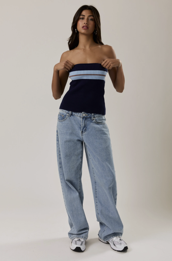 Woman wearing a strapless top with horizontal stripes and light blue jeans on a plain background
