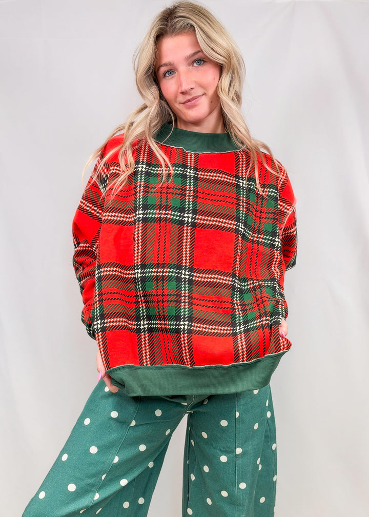 Woman wearing red and green plaid mock neck sweatshirt with green polka dot barrel pants on plain background