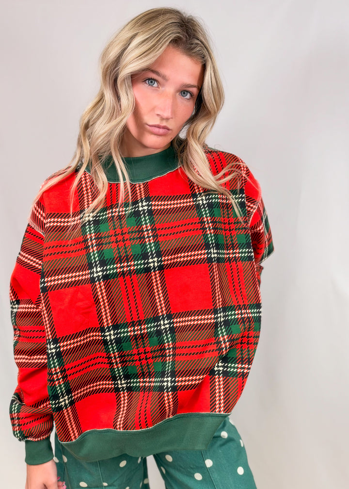Woman wearing red and green plaid mock neck sweatshirt with green polka dot pants on plain background
