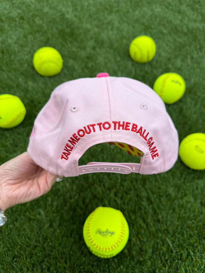 Pink cap with red text on a grass background with tennis balls