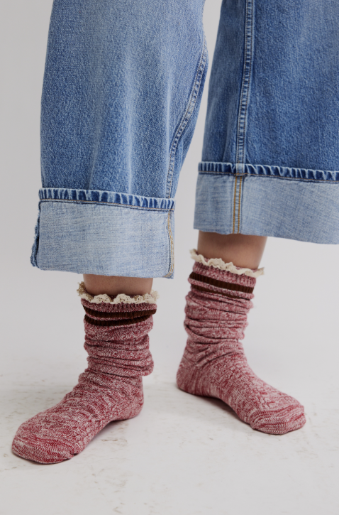 Person wearing pink textured socks with ruffled top and rolled-up blue jeans on a light background