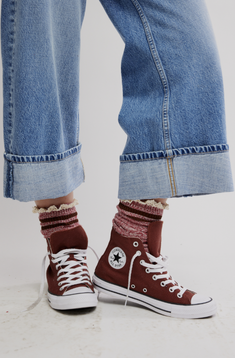 Person wearing maroon high-top sneakers with white laces, rolled-up blue jeans, and patterned socks on a light background.