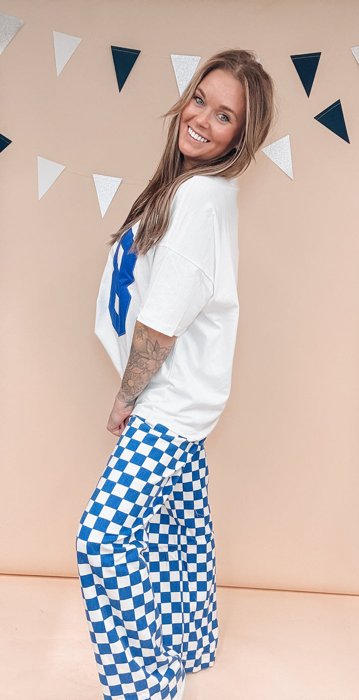 Woman wearing white tee and blue and white checker pants on plain background
