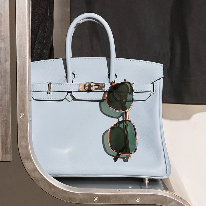 Light blue handbag with sunglasses on a metallic surface