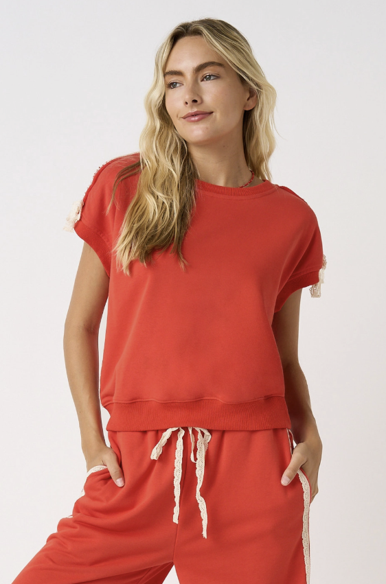 A woman modeling a matching rust-orange lounge set consisting of a short-sleeve crewneck sweatshirt and drawstring sweatpants against a plain white studio background.