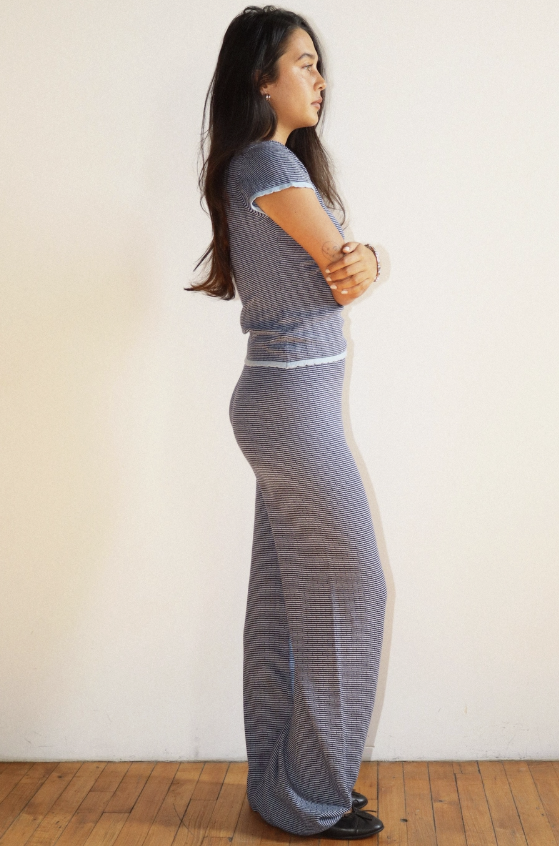 Woman wearing a gray knitted outfit standing against a white wall.