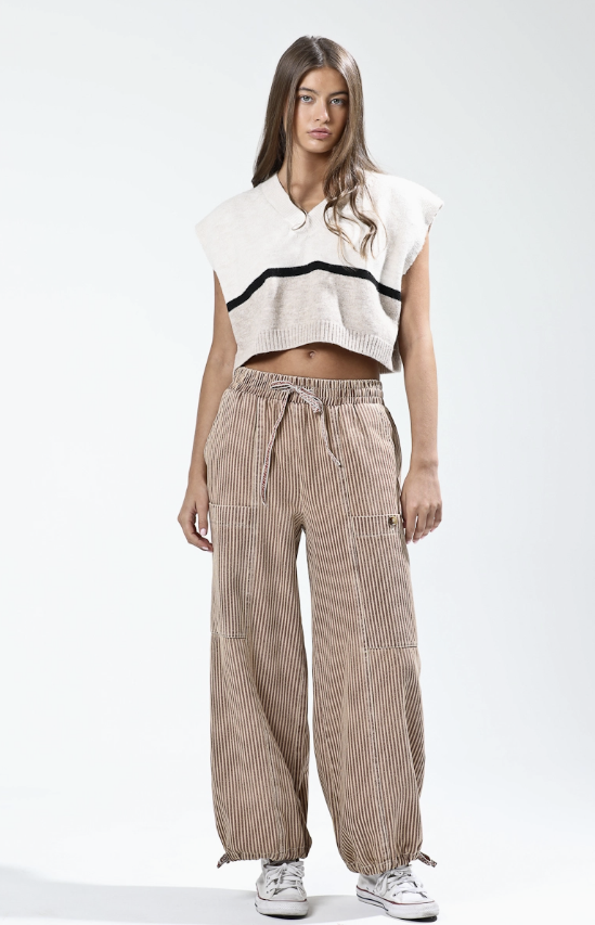 Woman wearing a white sleeveless top with black trim and striped pants on a white background