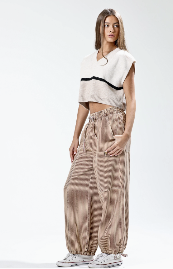 Woman wearing a white and black top with beige striped pants on a white background