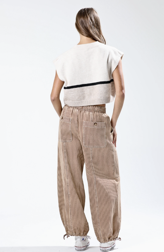 Woman wearing a white sleeveless top with black trim and beige striped pants on a white background