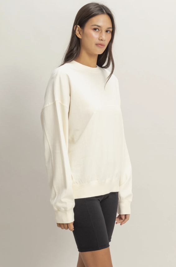 Woman wearing a cream sweater and black shorts on a plain background