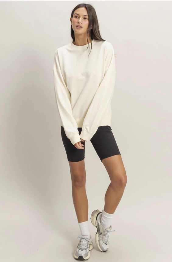 Woman wearing a white sweater and black shorts on a plain background