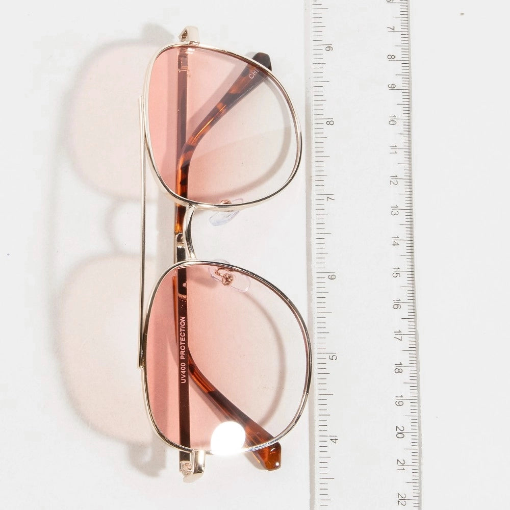 Sunglasses with rose gold frame and lenses next to a ruler on a white background