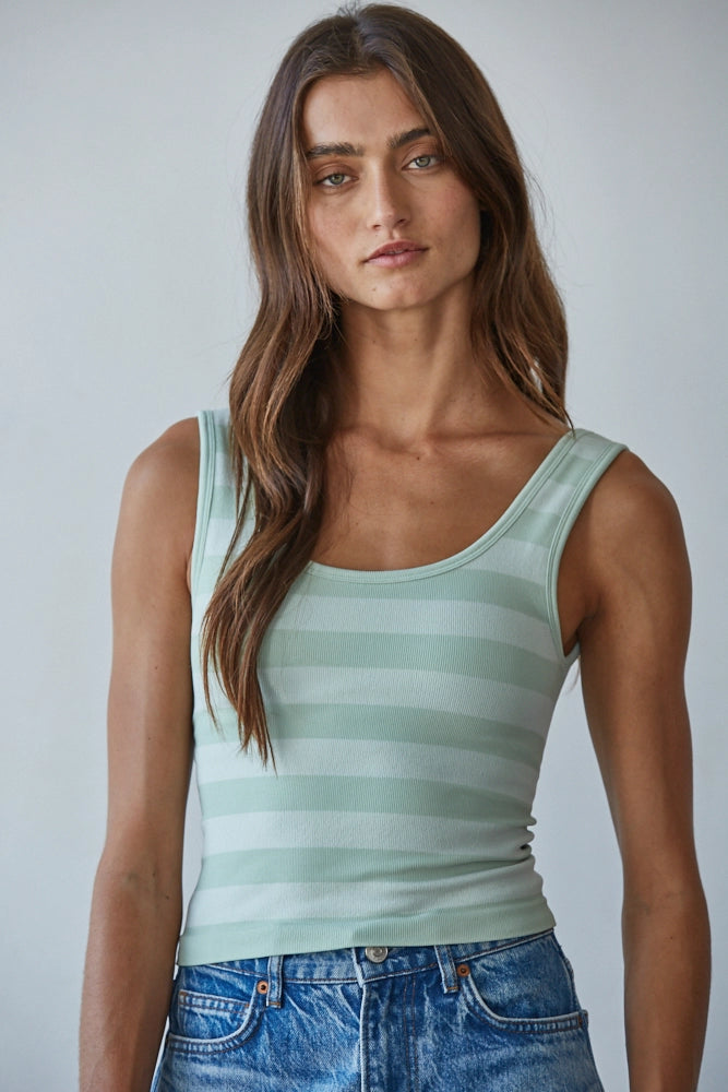 Woman wearing a green striped tank top and blue jeans against a plain background