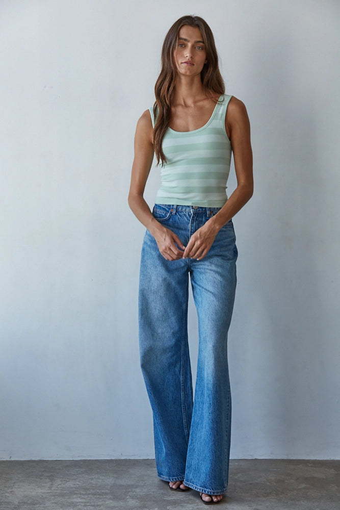 Woman wearing a light green tank top and blue jeans against a plain background