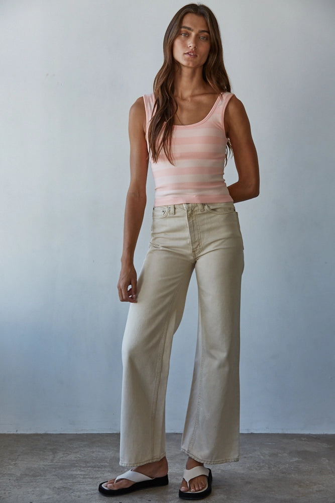 Woman wearing a striped tank top and beige pants against a plain background