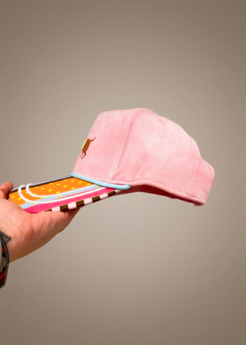 Side of pink faux suede trucker hat with striped bill on plain background