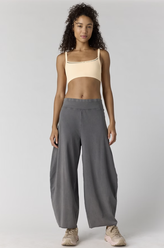 Woman wearing grey pants and yellow sports bra on plain background