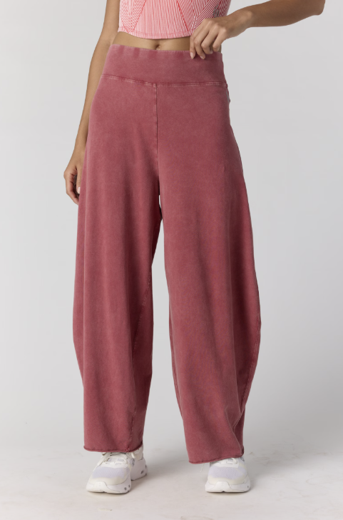 A person wearing dusty rose wide-leg sweatpants with a matching elastic waistband, paired with a pink striped crop top and white sneakers, shown against a light gray studio background.
