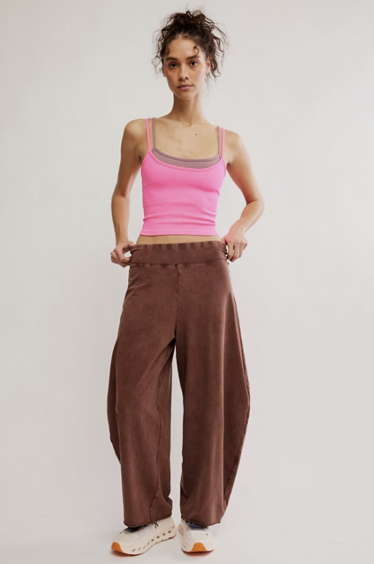 A model wearing brown wide-leg corduroy pants, a bright pink ribbed tank top, and white sneakers, standing against a light gray studio background.