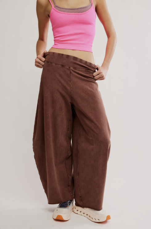 A model wearing a pair of wide-leg brown corduroy pants, styled with a pink tank top and white sneakers, against a light gray studio background.