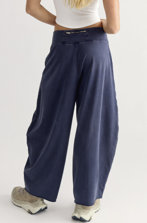 A person shown from the back wearing loose, wide-leg navy pants with a white ribbed crop top and beige sneakers against a plain light gray studio background.