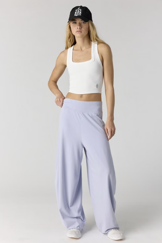 Woman wearing white tank and purple pants on plain background