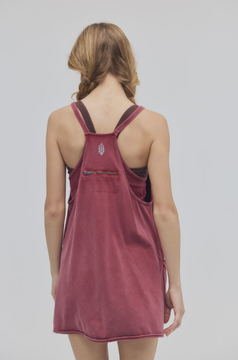 A woman viewed from behind wearing a dusty rose corduroy pinafore dress with dark red straps and a small silver emblem on the back.