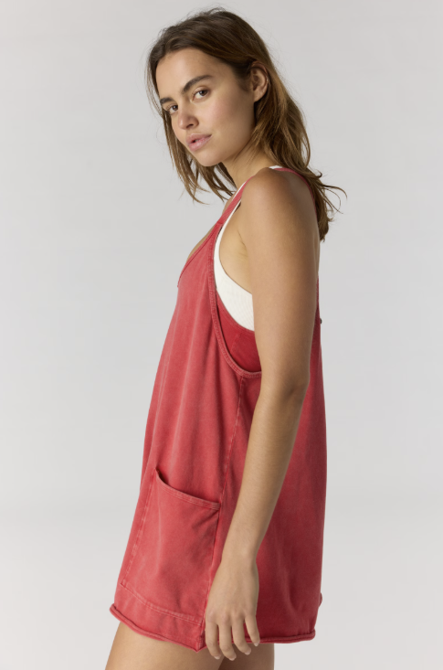 A woman wearing a washed red sleeveless tank dress over a white tank top, photographed against a light gray studio background.