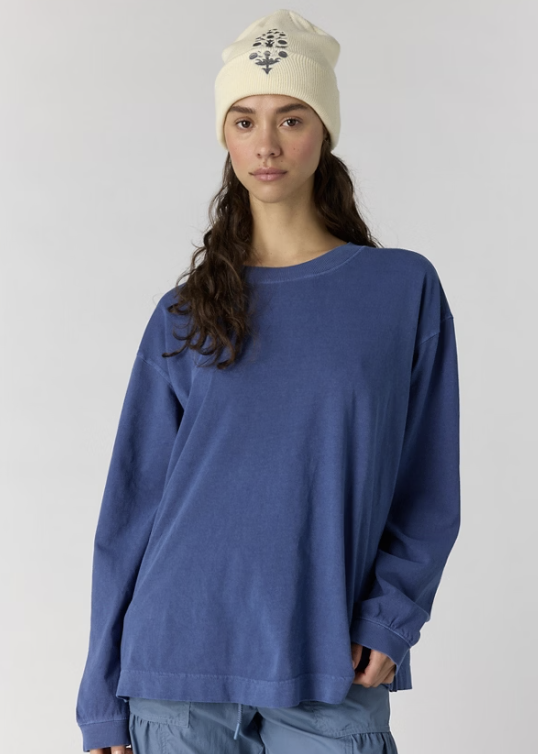 Woman wearing oversize blue long sleeve top and blue pants with white beanie on plain background