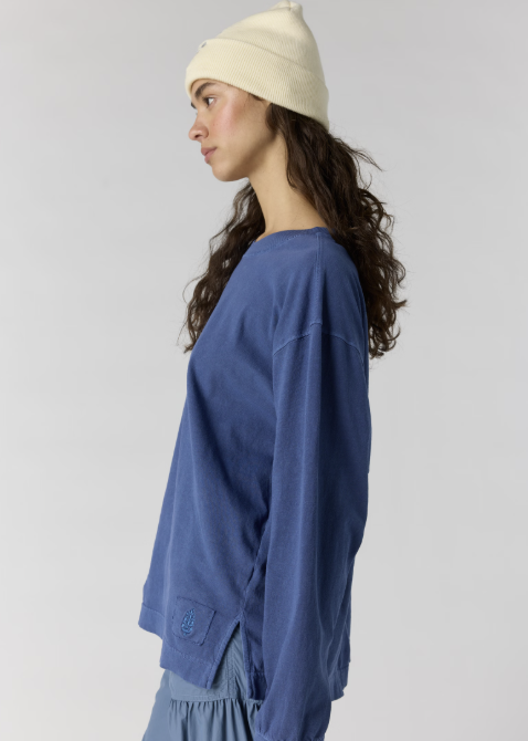 Woman wearing blue long sleeve top and blue pants with white beanie on plain background
