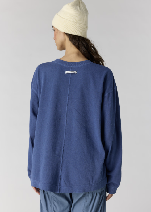 Woman shown from back wearing oversize blue long sleeve top and blue pants with white beanie on plain background