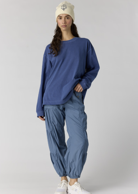 Woman wearing oversize long sleeve blue top and blue pants with white beanie on plain background