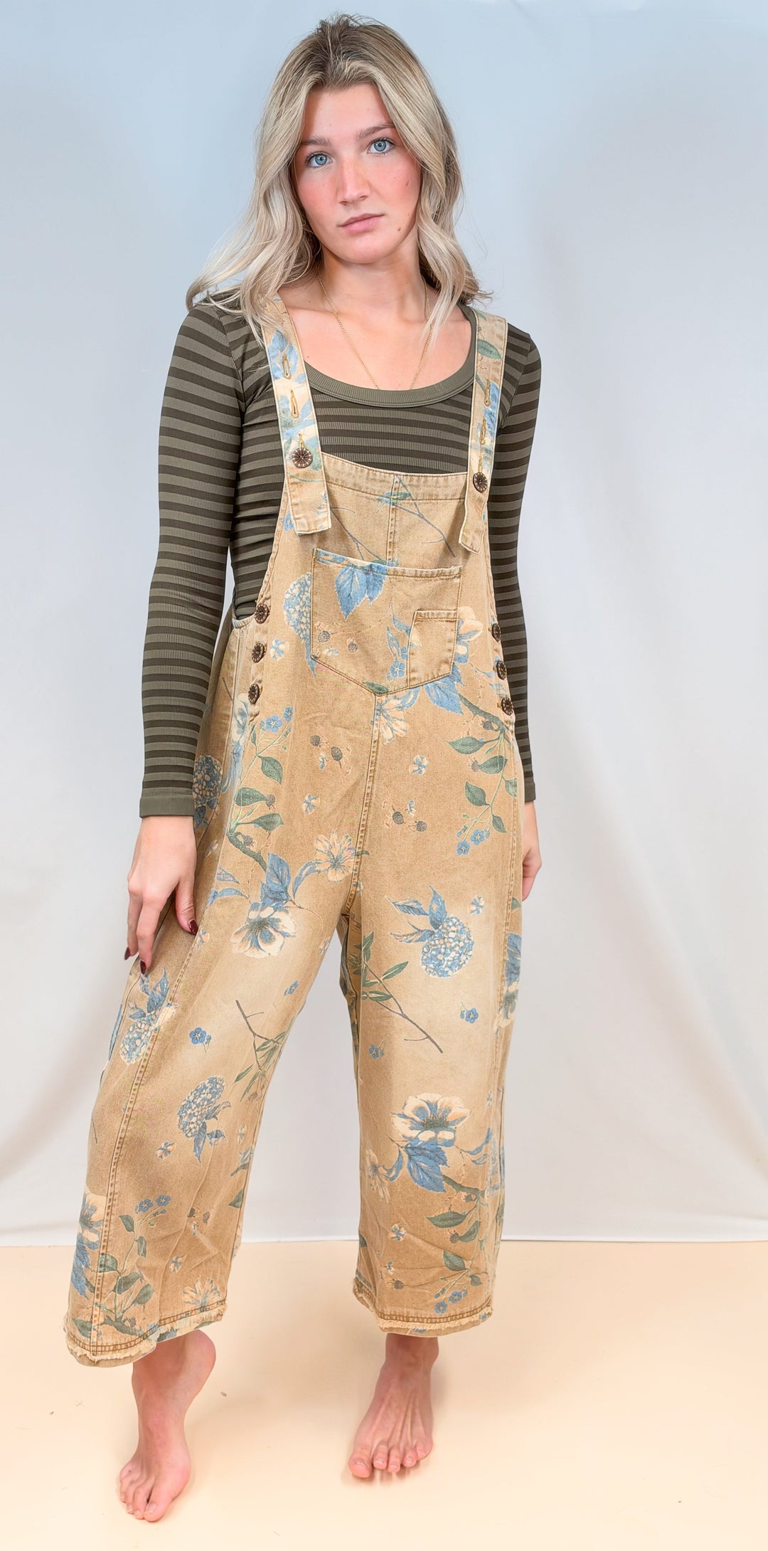Woman wearing beige floral overalls with green stripe long sleeve on plain background