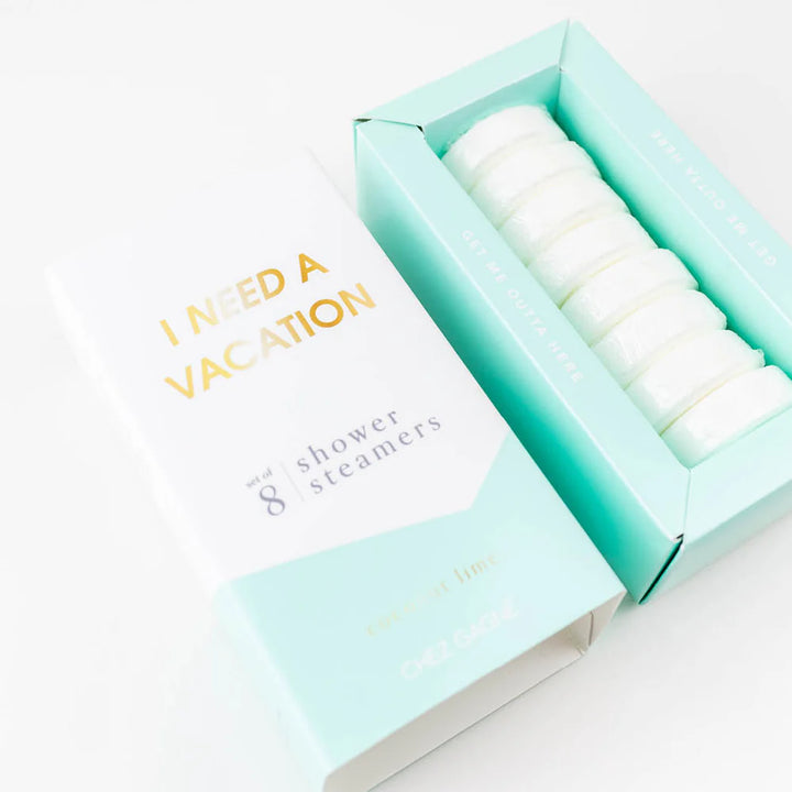 An open mint green box of shower steamers next to its white and mint green packaging sleeve. The packaging features gold foil text reading &