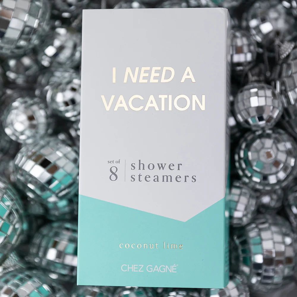 A rectangular product box for shower steamers stands upright against a background of reflective silver disco balls. The box is white on the upper half with pale yellow text reading &