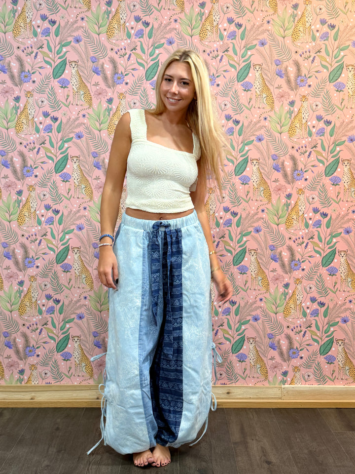 Woman wearing cream tank and blue balloon pants on pink floral background