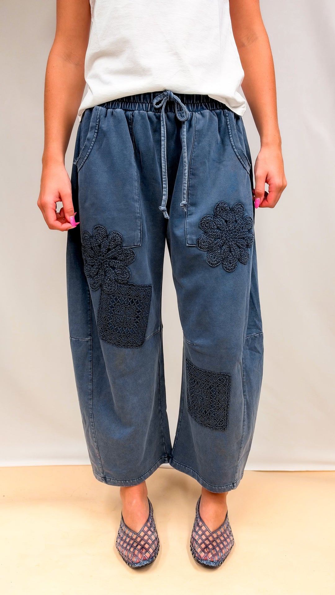 Woman wearing blue barrel sweatpants with crochet details and white tee on plain background