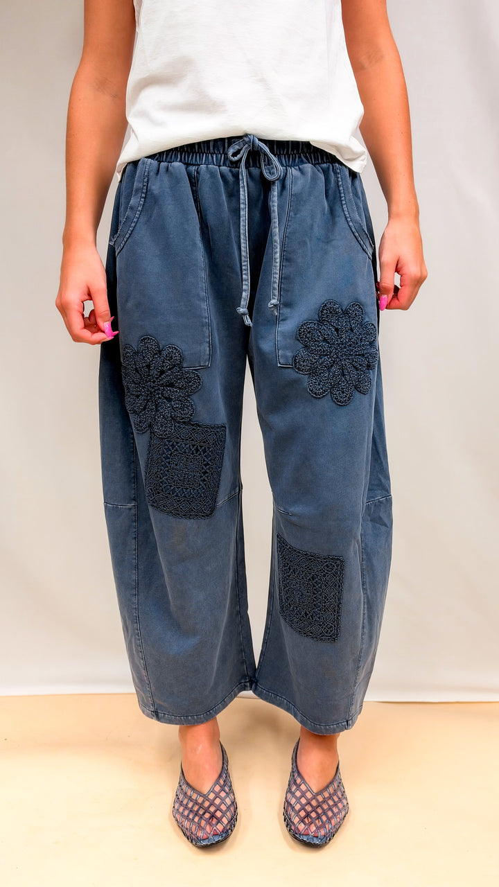 Woman wearing blue barrel sweatpants with crochet details and white tee on plain background