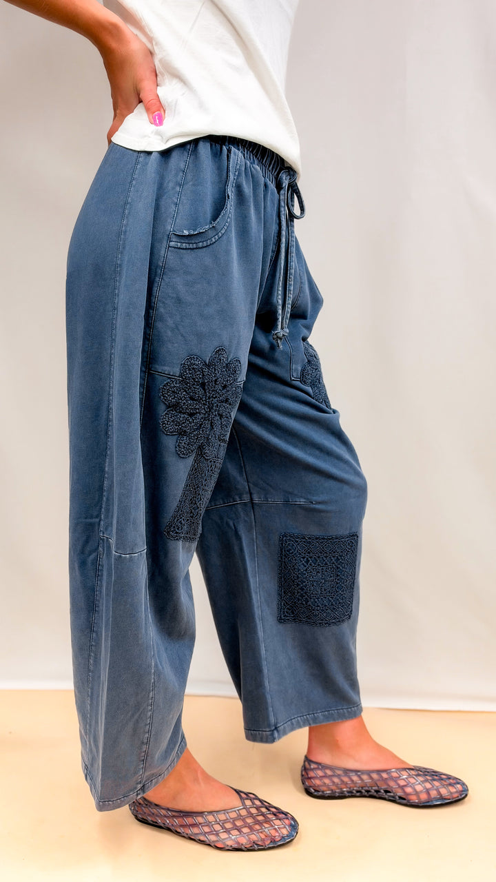 Woman wearing blue barrel sweatpants with crochet details and white tee on plain background