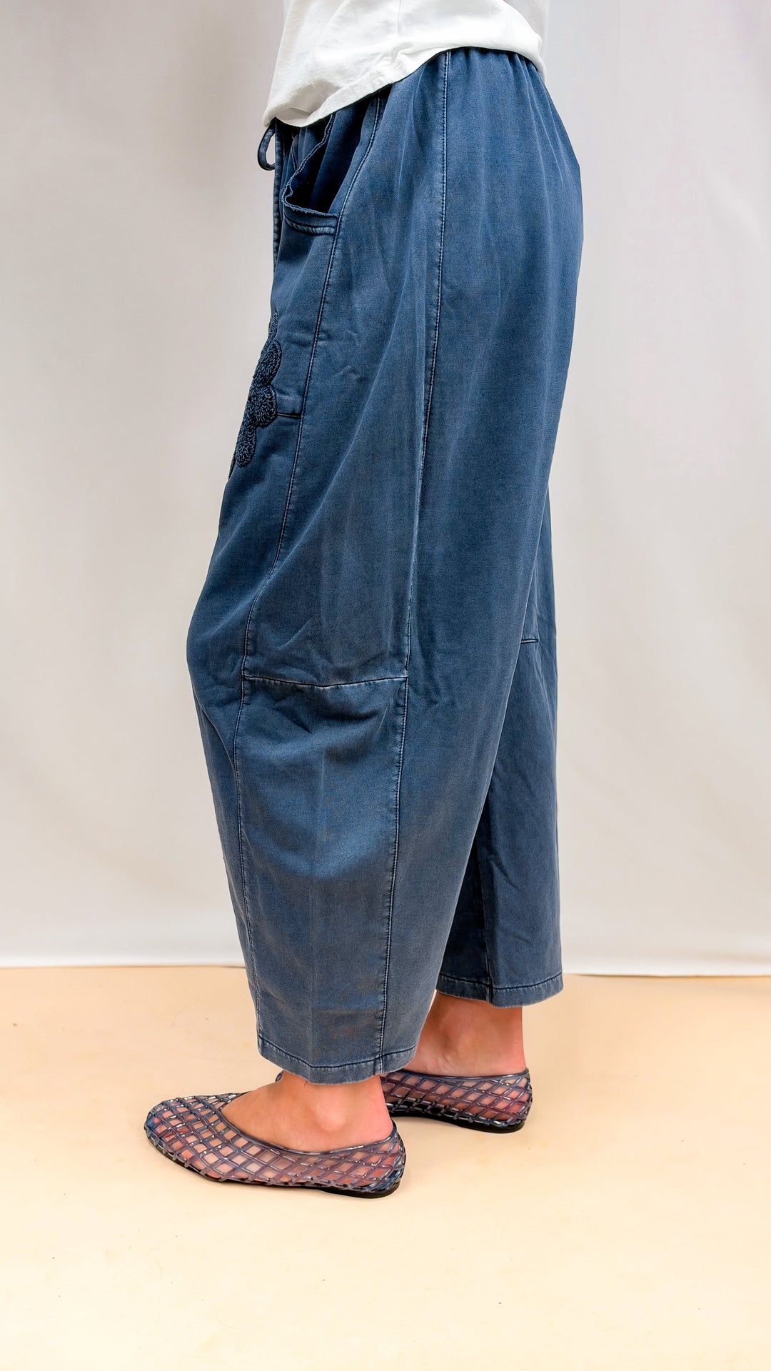 Woman wearing blue barrel sweatpants with crochet details and white tee on plain background