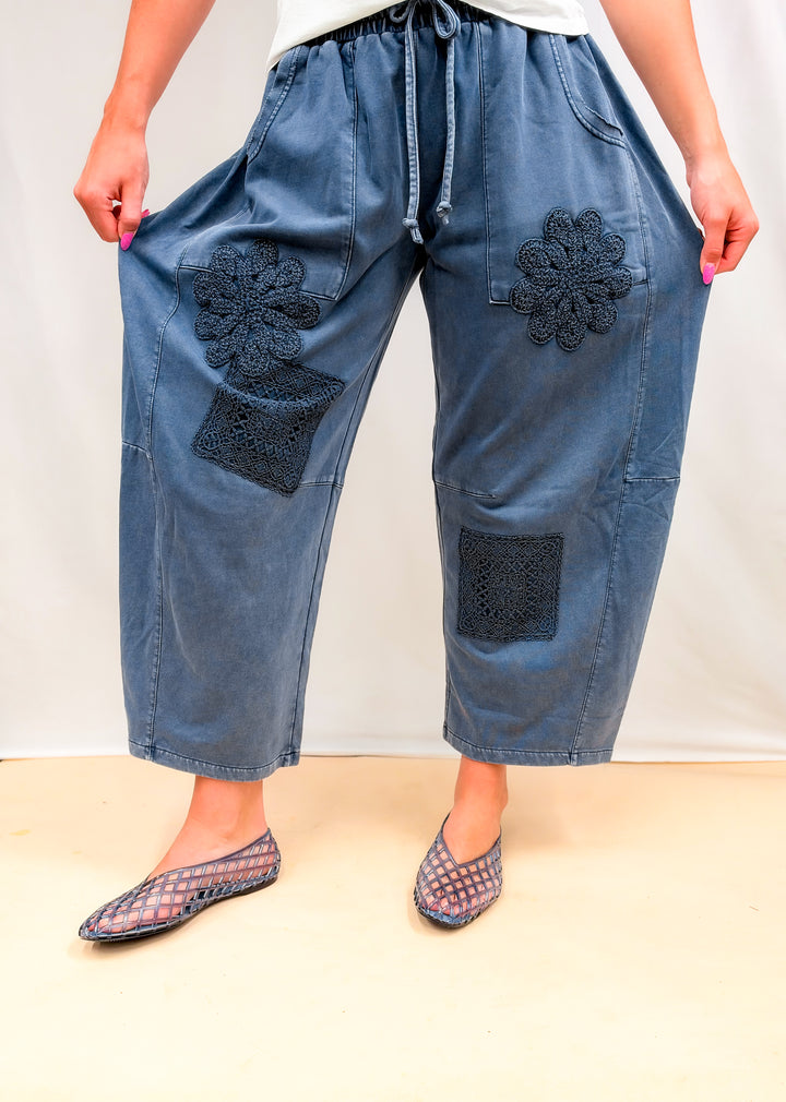 Woman wearing blue barrel sweatpants with crochet details and white tee on plain background