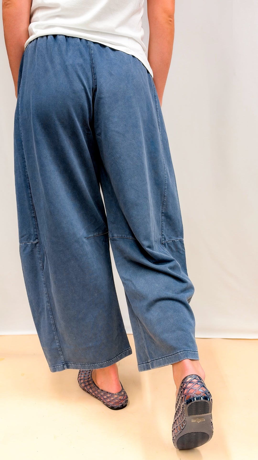 Woman shown from back wearing blue barrel sweatpants and white tee on plain background