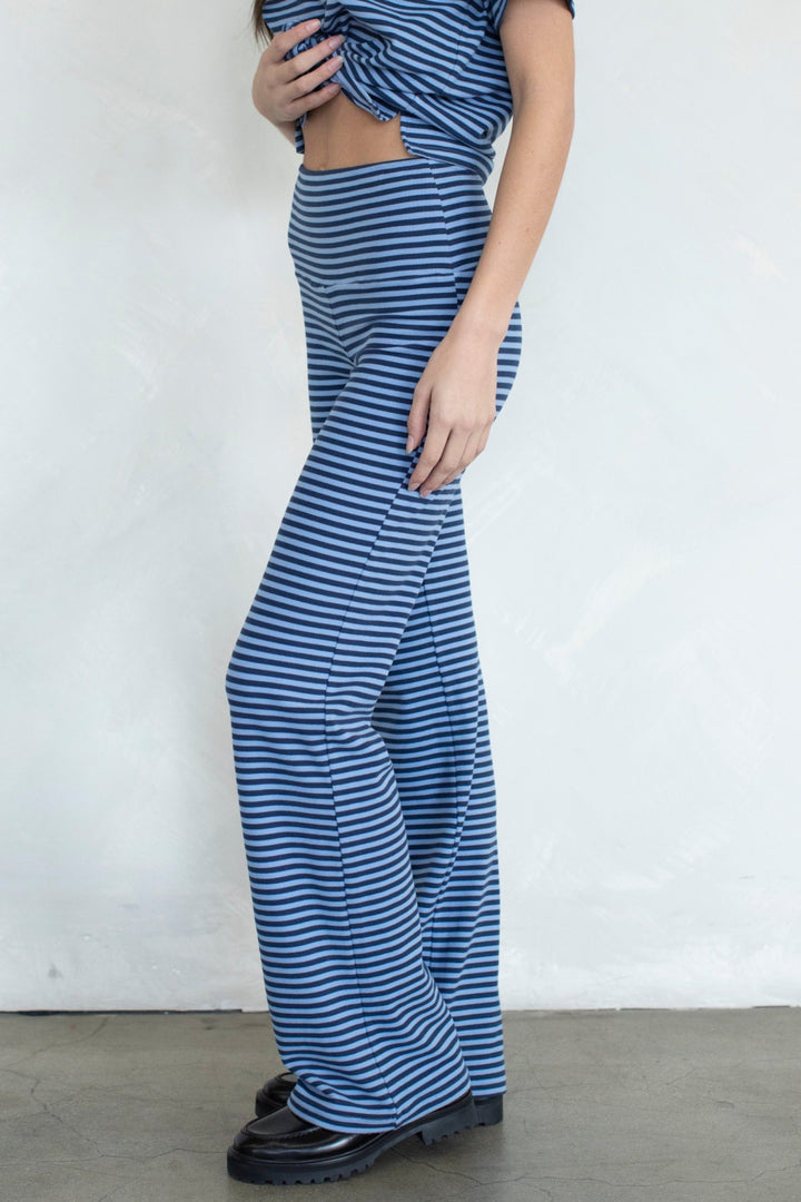 A model wearing a matching two-piece set consisting of blue and white horizontally striped wide-leg pants and a cropped top with side cutouts, paired with black platform shoes against a plain white wall.