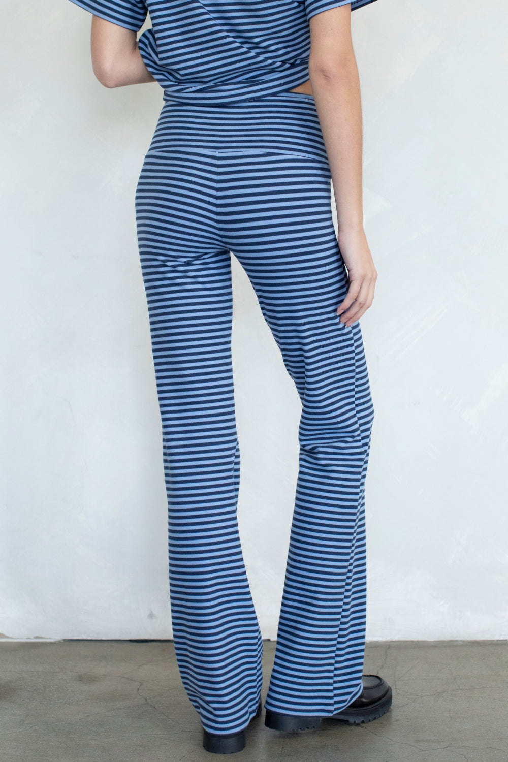 A person shown from the back wearing blue and white horizontally striped flared pants and a matching striped top, standing against a plain light wall.
