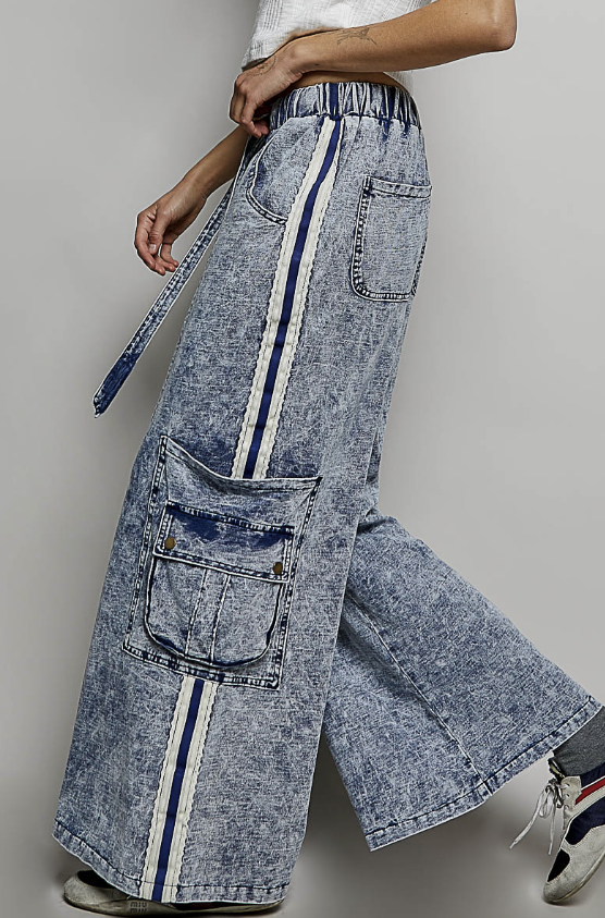 A person wearing wide-leg acid-wash denim cargo pants with vertical navy and white stripes down the sides, shown from the waist down against a plain light gray studio background.