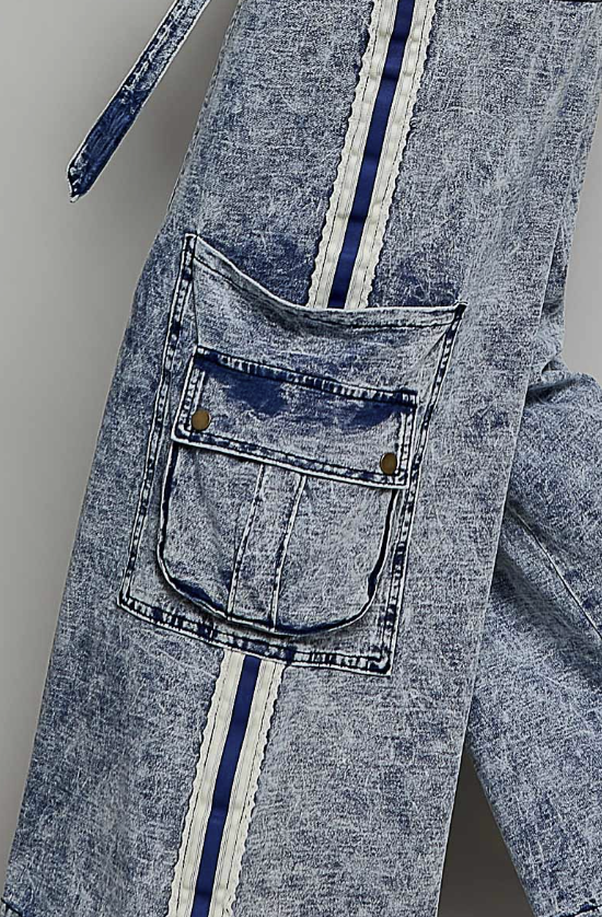 Close-up of a pair of blue acid-wash denim pants featuring a large front cargo pocket with brass buttons and a vertical white and navy stripe running down the side.