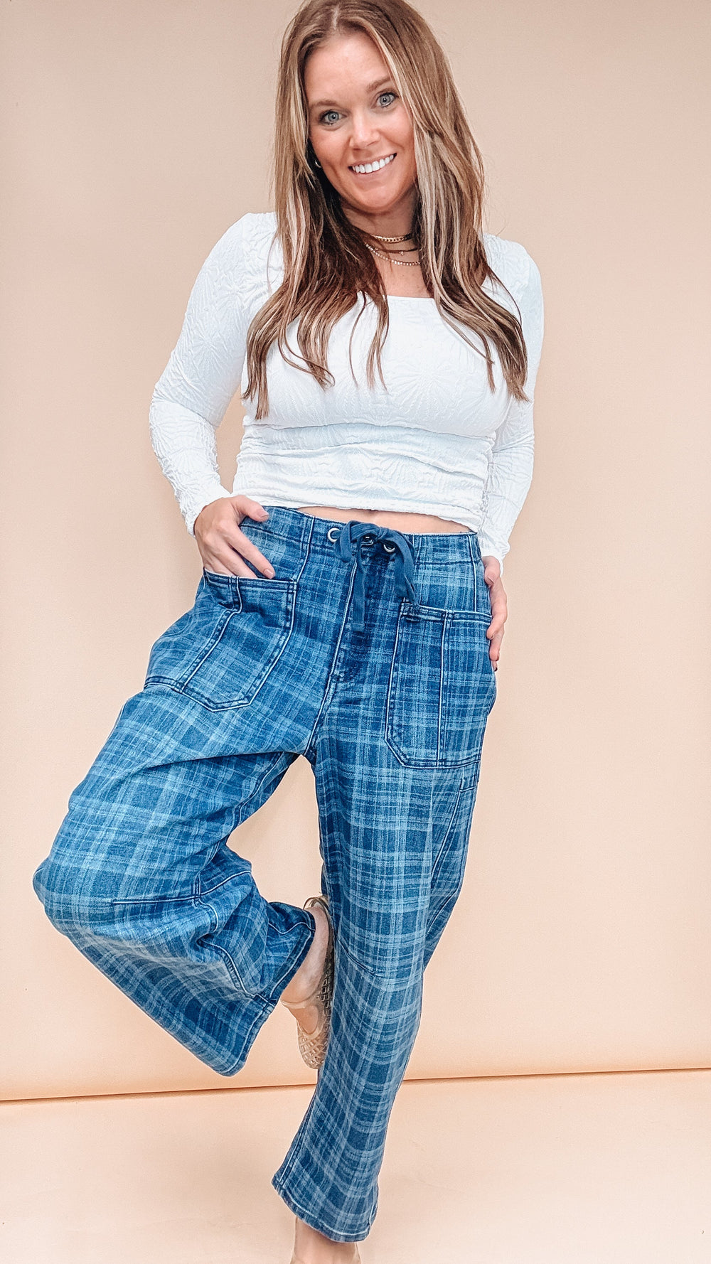 Woman wearing blue plaid pants with white long sleeve top on plain background