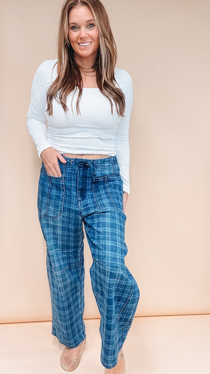 A woman modeling a white ribbed long-sleeve crop top and blue plaid wide-leg pants against a solid beige studio backdrop.
